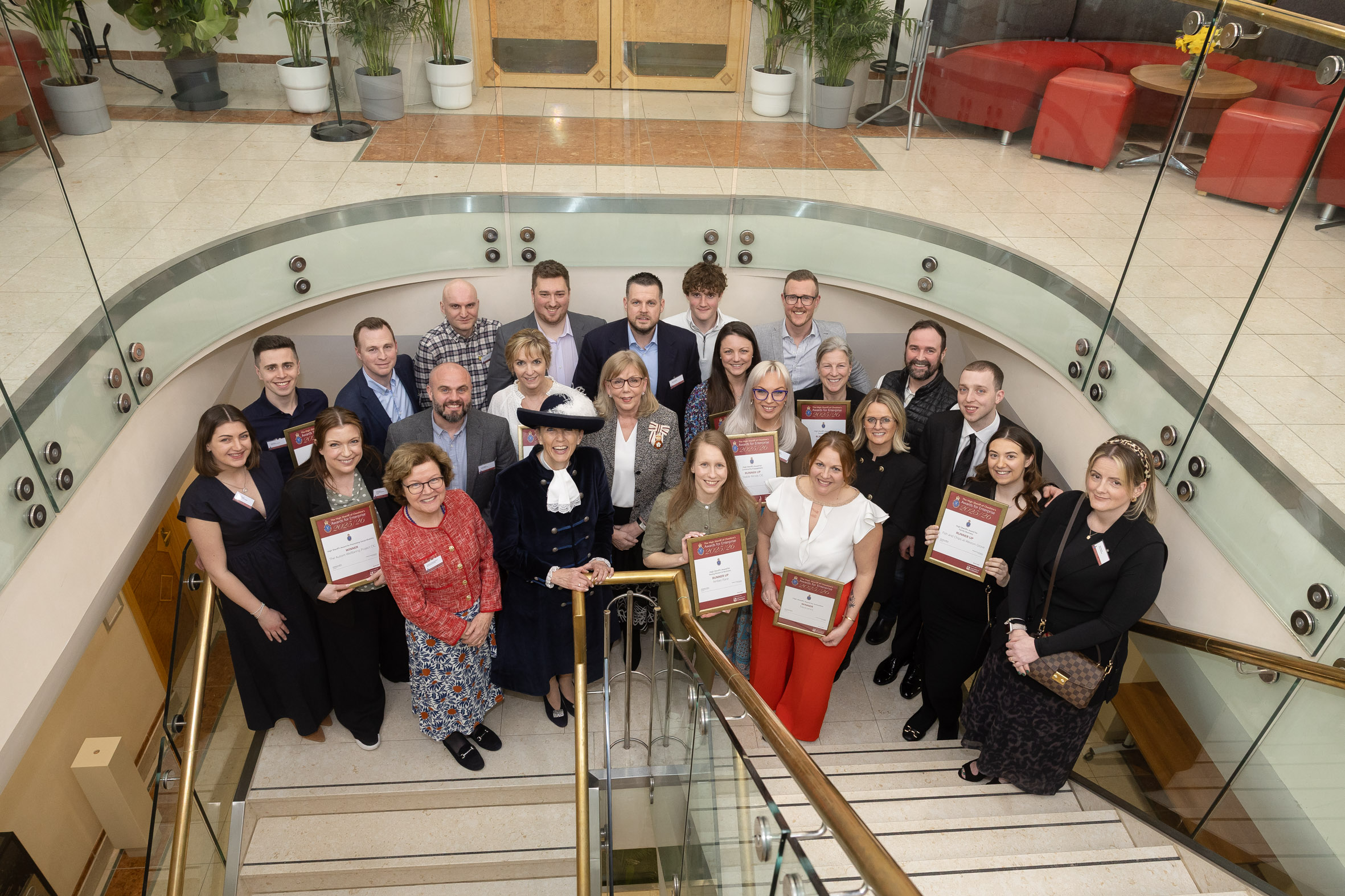 A group of people on a stairway, smiling, as winners and runners-up of the High Sheriff of Cheshire Awards for Enterprise.